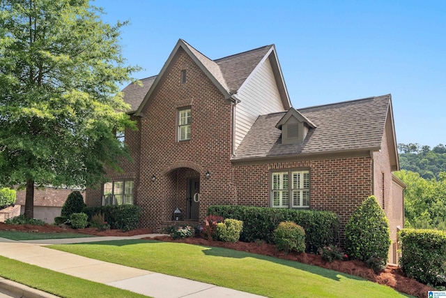 tudor home with brick siding, a front lawn, and roof with shingles