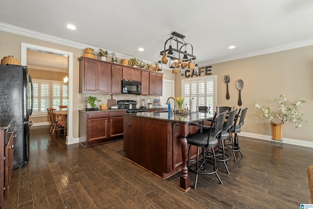 kitchen featuring black appliances, dark wood finished floors, a center island with sink, baseboards, and crown molding