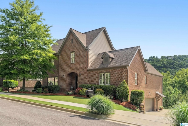 view of front of house featuring brick siding, an attached garage, driveway, and roof with shingles