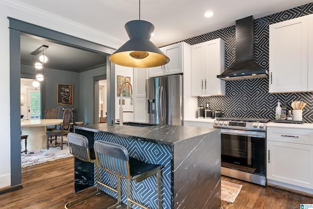 kitchen featuring appliances with stainless steel finishes, wall chimney range hood, dark wood-style flooring, white cabinets, and crown molding