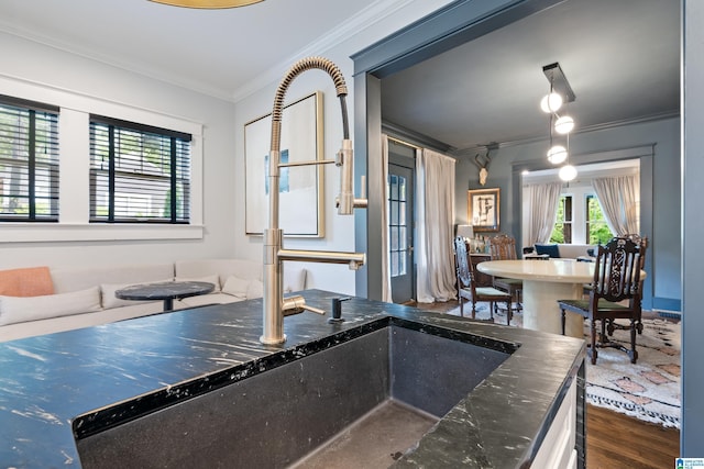 kitchen featuring crown molding, wood finished floors, dark stone counters, and a sink