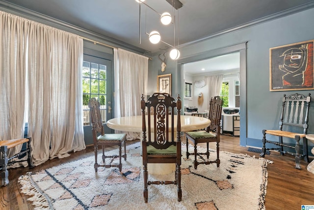 dining space with crown molding, wood finished floors, and plenty of natural light