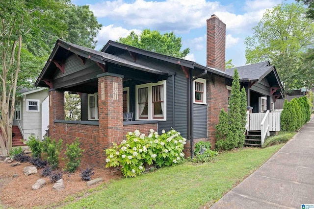 view of property exterior featuring a chimney, a lawn, brick siding, and covered porch