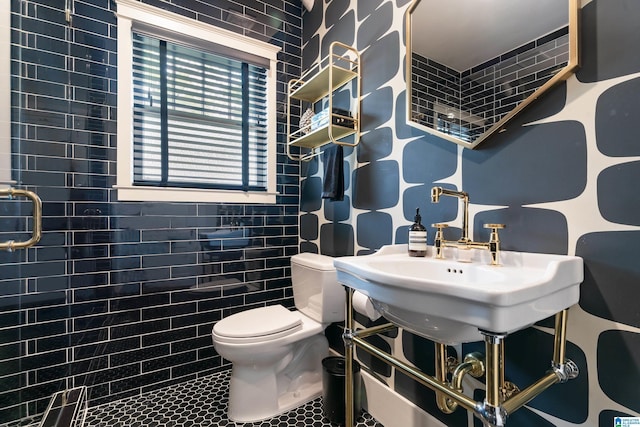 bathroom with toilet, tiled shower, and a sink
