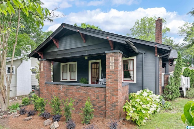 view of front facade with a chimney, covered porch, and brick siding