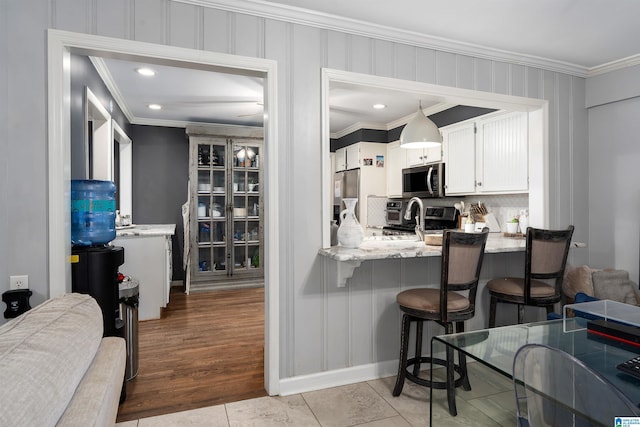 734 Crest Ln, Homewood, AL 35209 - kitchen with crown molding, backsplash, stainless steel appliances, white cabinetry, and a breakfast bar