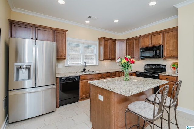 kitchen featuring black appliances, a sink, a kitchen island, a breakfast bar area, and light stone countertops