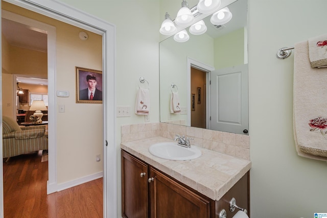 ensuite bathroom featuring wood finished floors, vanity, a chandelier, and baseboards