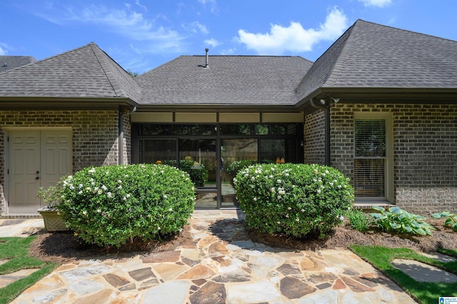 rear view of property featuring roof with shingles, brick siding, and a sunroom