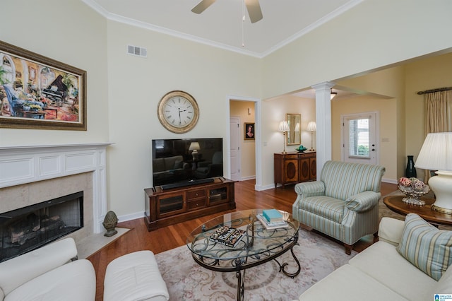 living area with decorative columns, ceiling fan, wood finished floors, crown molding, and a premium fireplace
