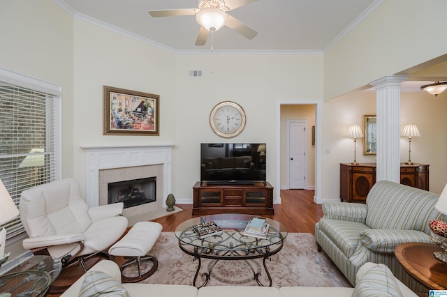 living room with ceiling fan, wood finished floors, crown molding, decorative columns, and a tile fireplace
