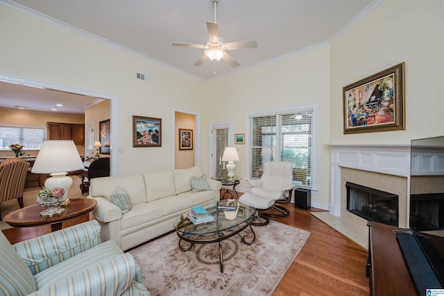 living area with crown molding, light wood-type flooring, a high end fireplace, ceiling fan, and baseboards