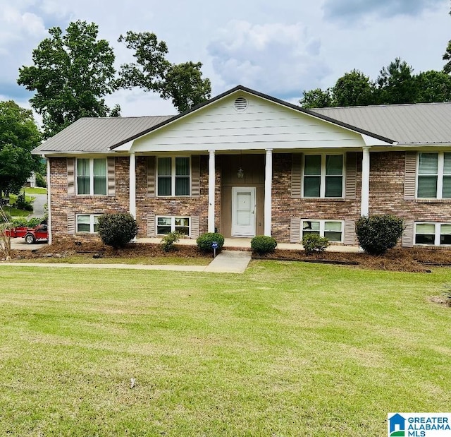 raised ranch with a front lawn, metal roof, and brick siding