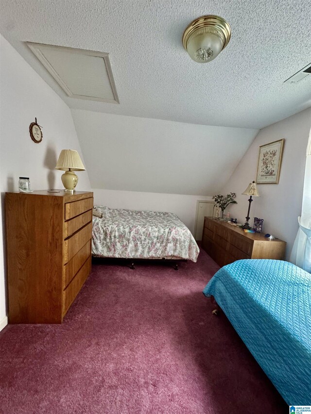 carpeted bedroom featuring lofted ceiling, attic access, and a textured ceiling