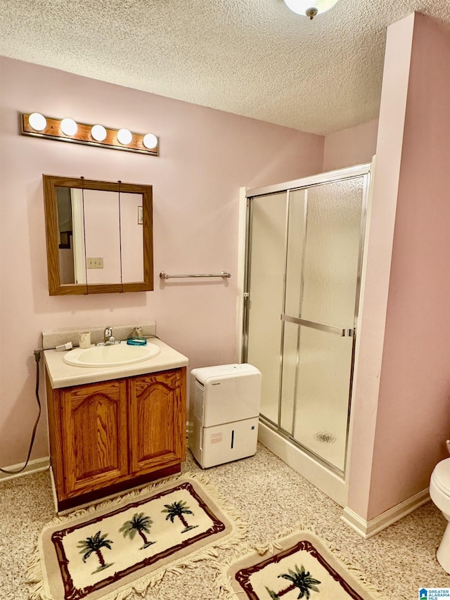 full bathroom with toilet, a textured ceiling, a shower stall, vanity, and baseboards