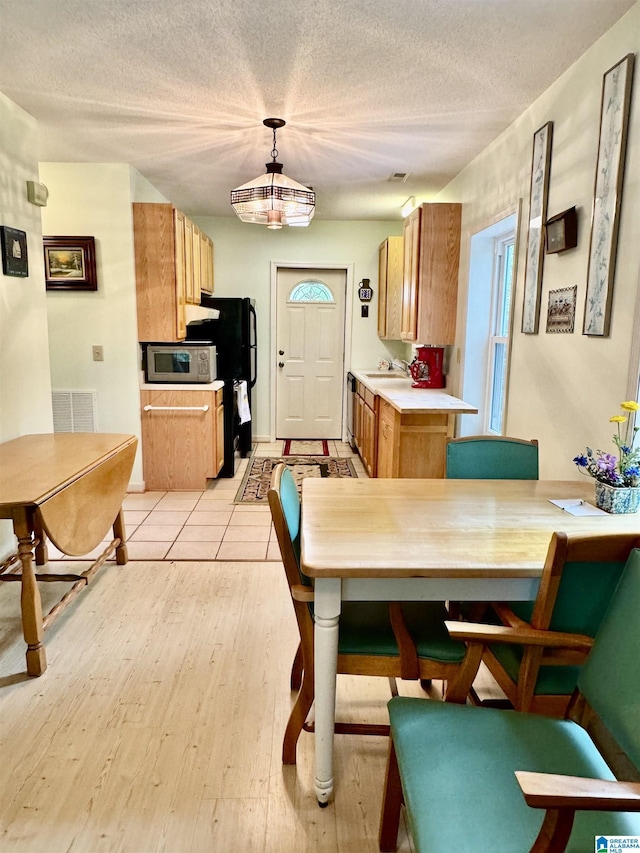 kitchen featuring stainless steel microwave, light countertops, light wood-type flooring, a sink, and brown cabinetry
