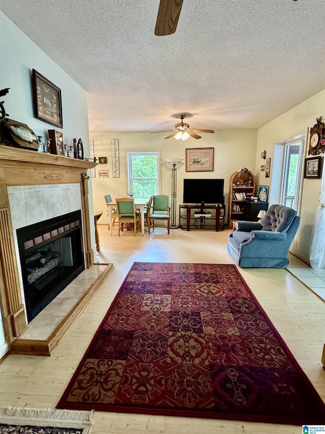 living area with ceiling fan, healthy amount of natural light, a textured ceiling, and a tile fireplace