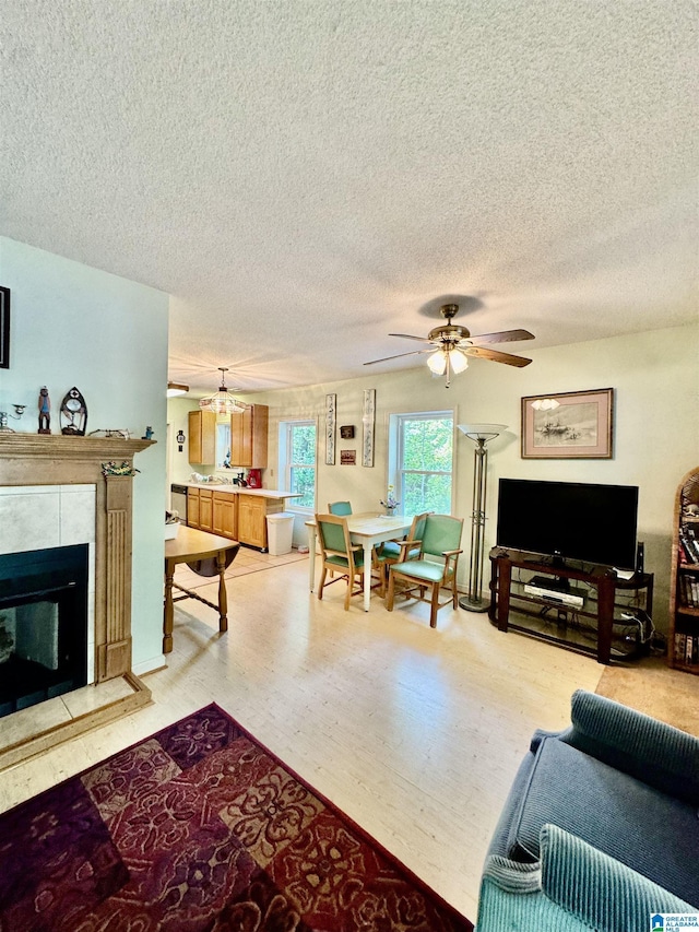 living room with a textured ceiling, a ceiling fan, light wood-style flooring, and a fireplace