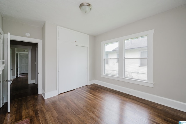unfurnished bedroom with baseboards, dark wood-style floors, and a closet