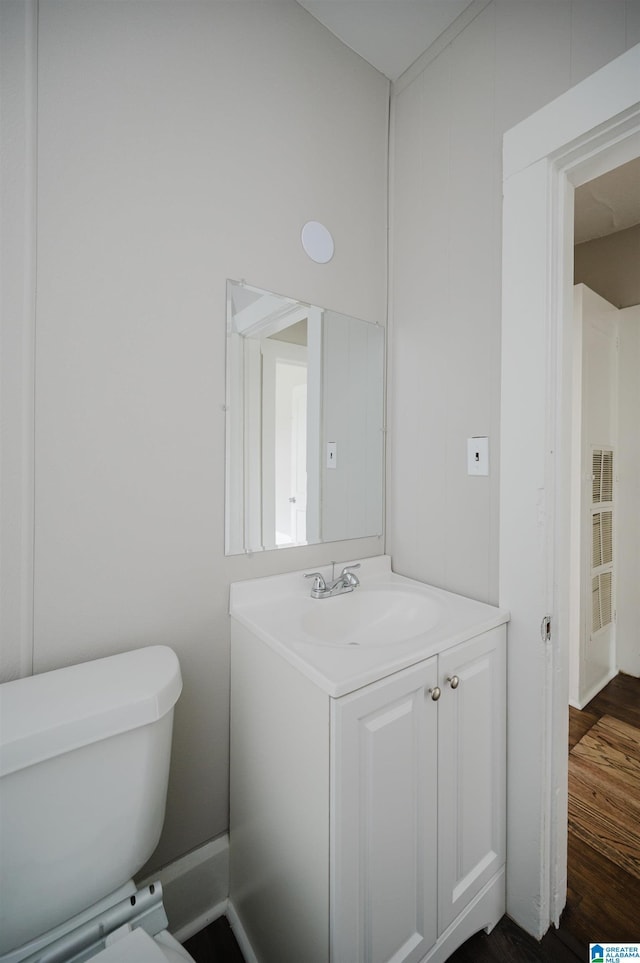 half bath with wood finished floors, toilet, and vanity