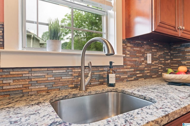 142 Falling Waters Ln, Maylene, AL 35114 - kitchen view of a sink, backsplash, brown cabinetry, and light stone countertops