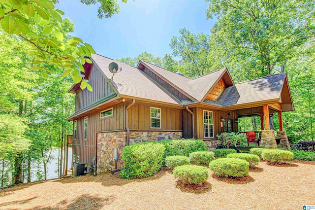view of front of house featuring board and batten siding, central air condition unit, roof with shingles, stone siding, and a porch