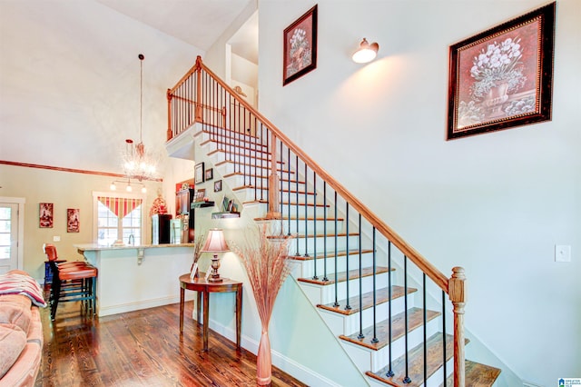 staircase featuring wood finished floors, a towering ceiling, a chandelier, and baseboards