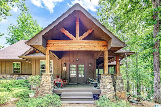 property entrance with board and batten siding, french doors, covered porch, roof with shingles, and stone siding