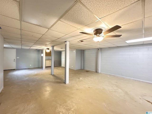 finished below grade area featuring concrete block wall, a drop ceiling, and ceiling fan