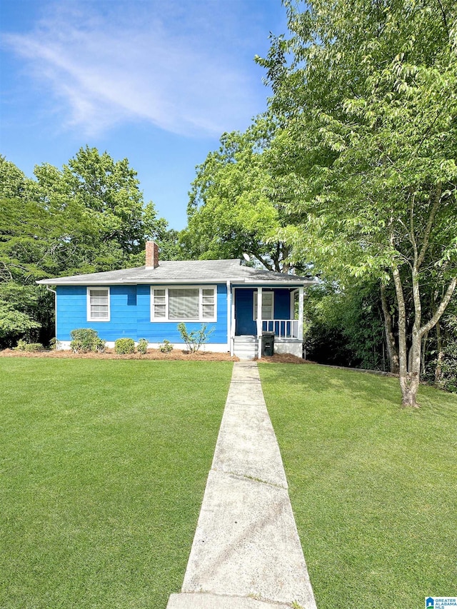 view of front of home with covered porch, a front lawn, and a chimney