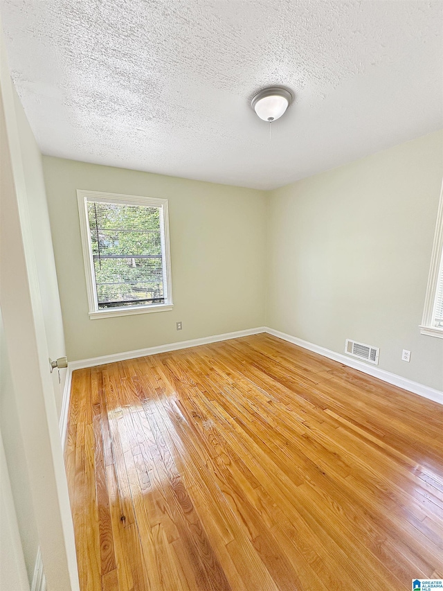 empty room with light wood-type flooring, a textured ceiling, and baseboards
