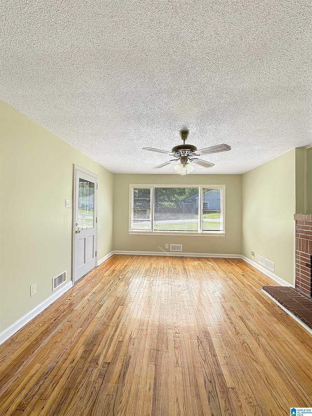 unfurnished living room with light wood-type flooring, a brick fireplace, a ceiling fan, baseboards, and a textured ceiling