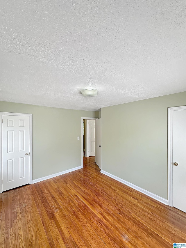 empty room with wood finished floors, baseboards, and a textured ceiling