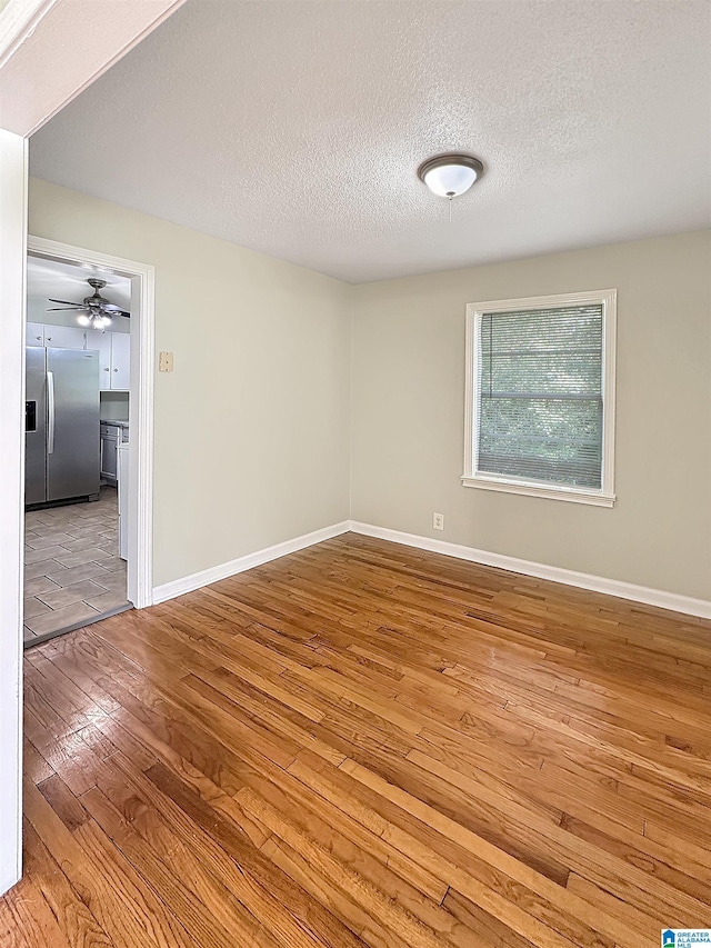 unfurnished room with wood-type flooring, baseboards, a textured ceiling, and a ceiling fan