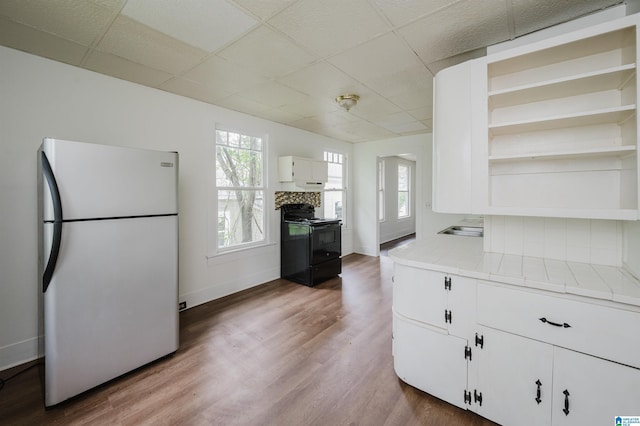 kitchen with freestanding refrigerator, open shelves, black range with electric cooktop, a drop ceiling, and white cabinetry