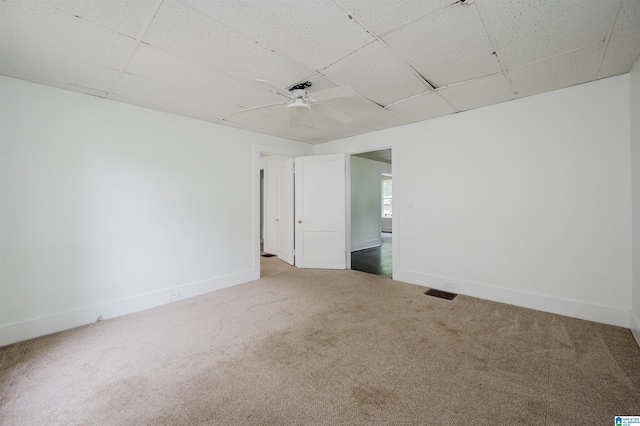 empty room with carpet floors, a drop ceiling, ceiling fan, and baseboards