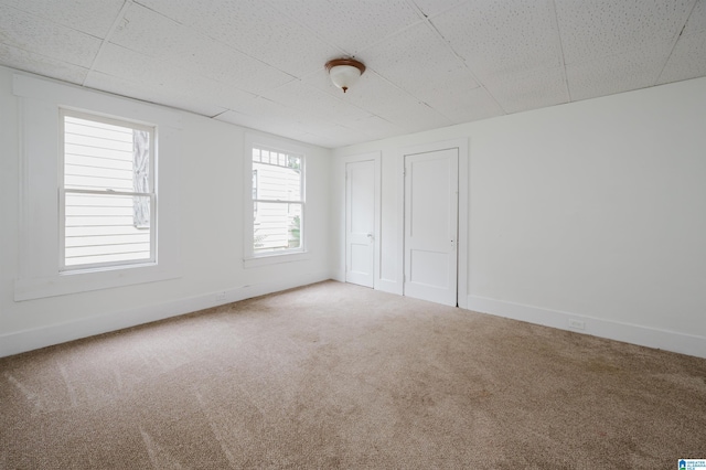 unfurnished bedroom with carpet floors, baseboards, multiple closets, and a paneled ceiling