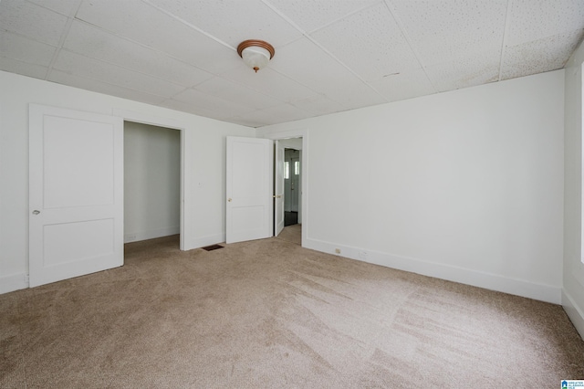 unfurnished bedroom featuring a drop ceiling, carpet, and baseboards