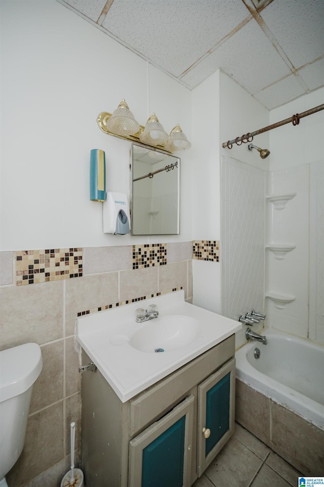 full bath with tile walls, toilet, vanity, a drop ceiling, and tiled shower / bath combo