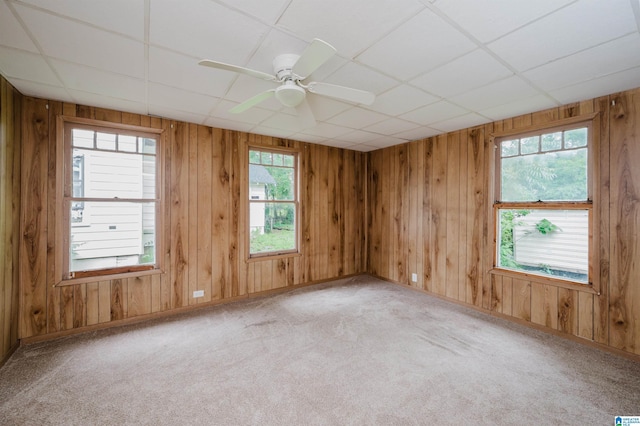 unfurnished room featuring carpet flooring, wooden walls, ceiling fan, a paneled ceiling, and baseboards