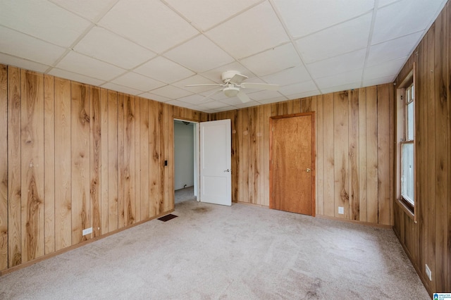 spare room with carpet flooring, wood walls, a ceiling fan, and a paneled ceiling