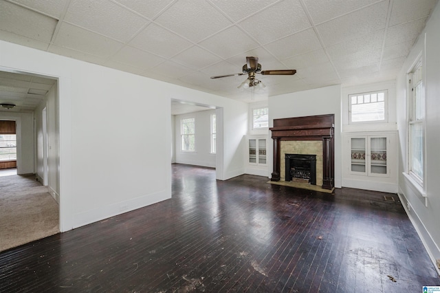 unfurnished living room with a ceiling fan, a fireplace, hardwood / wood-style flooring, healthy amount of natural light, and a drop ceiling