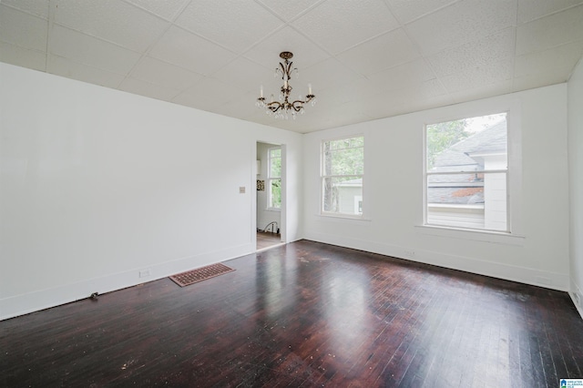 unfurnished room with hardwood / wood-style floors, baseboards, a drop ceiling, and a chandelier