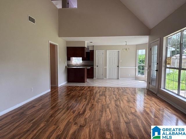 7601 Meadows Dr S, Mobile, AL 36619 - unfurnished living room with a chandelier, dark wood finished floors, high vaulted ceiling, baseboards, and a sink