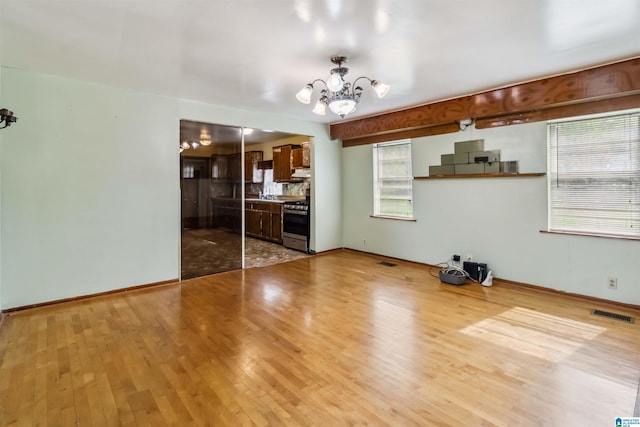 unfurnished living room with a chandelier, wood finished floors, and baseboards