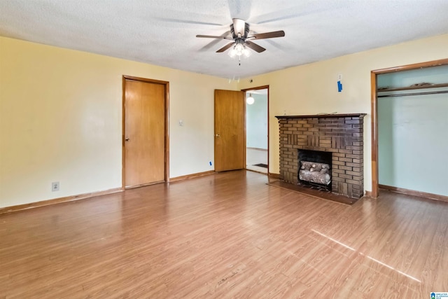 unfurnished living room with a ceiling fan, wood finished floors, a fireplace, baseboards, and a textured ceiling
