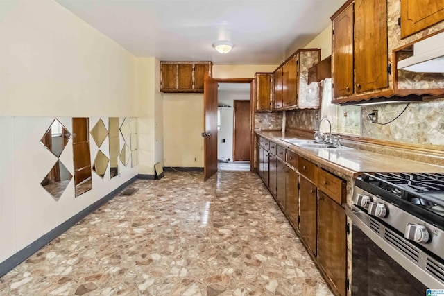 kitchen with a sink, stainless steel range with gas cooktop, brown cabinetry, backsplash, and under cabinet range hood