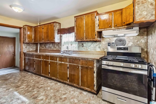 kitchen featuring stainless steel range with gas cooktop, under cabinet range hood, a sink, backsplash, and brown cabinetry