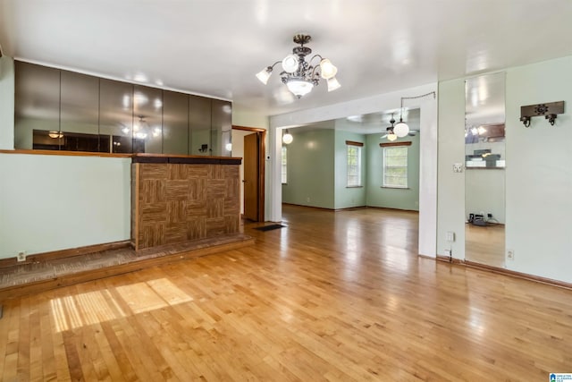 unfurnished living room featuring a chandelier, light wood-type flooring, ceiling fan, and baseboards