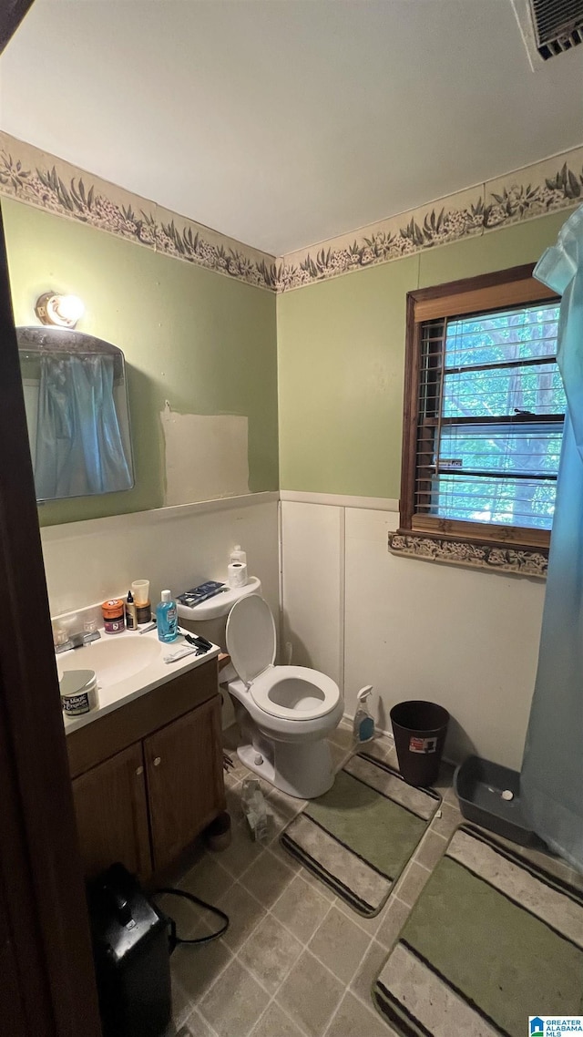 813 W 8th St, Sylacauga, AL 35150 - bathroom featuring a wainscoted wall, vanity, toilet, a decorative wall, and tile patterned floors